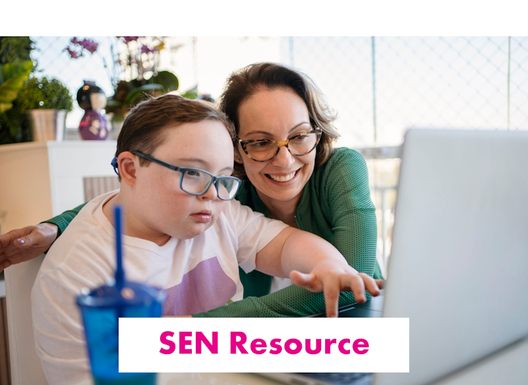 Boy sat typing on a laptop, aided by a smiling adult