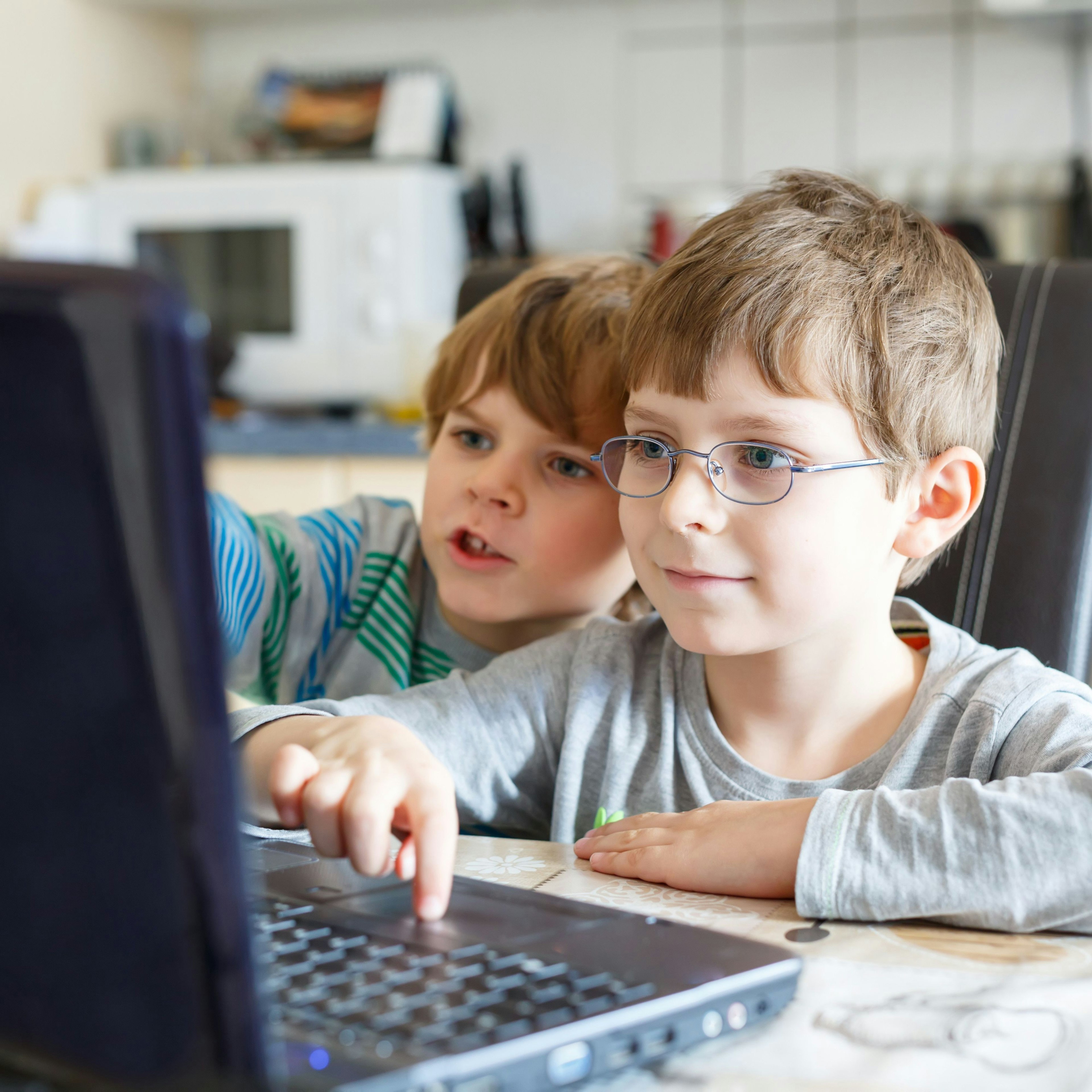 Two young boys typing on a laptop.