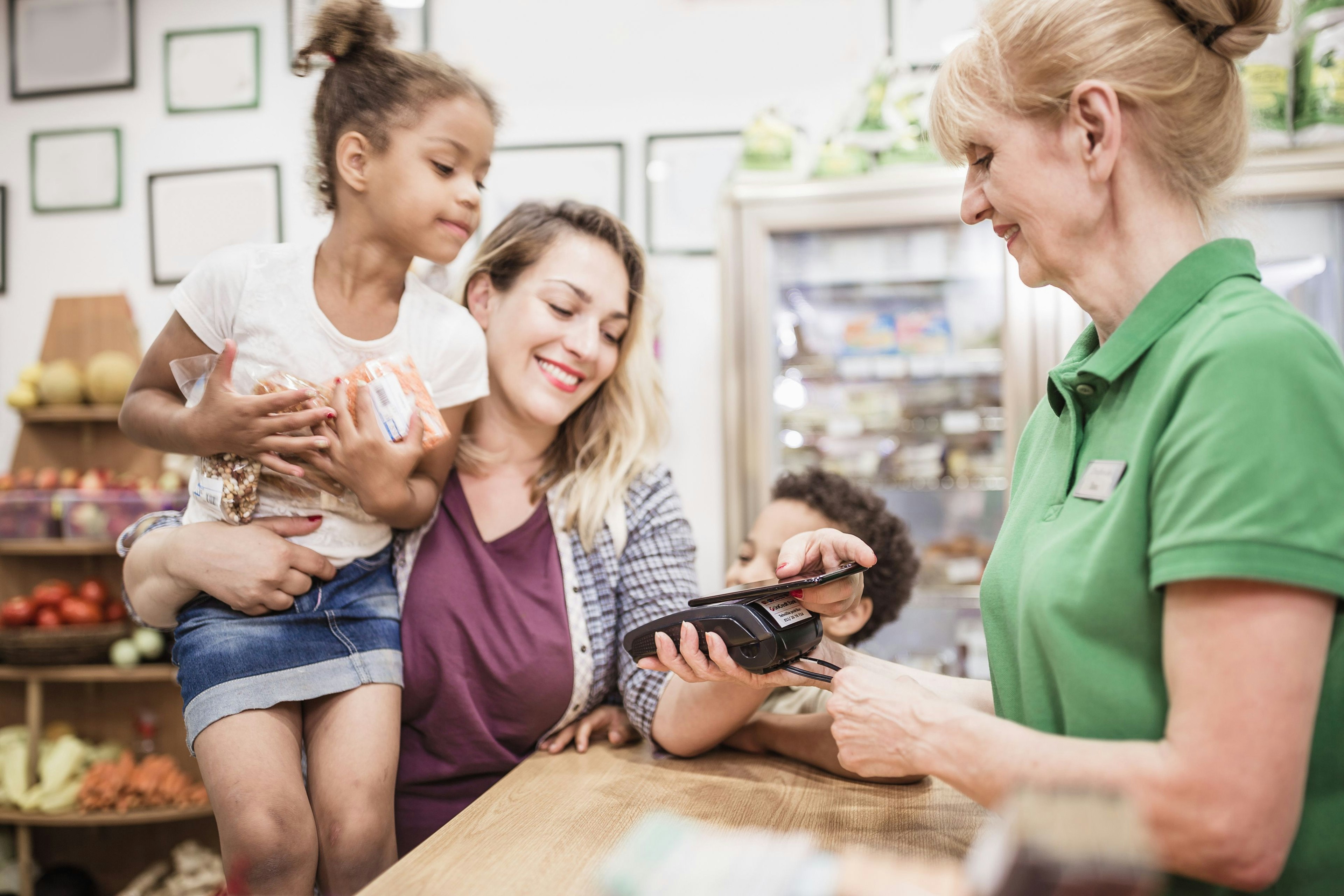 A mother and daughter pay a shop keeper using a card machine.