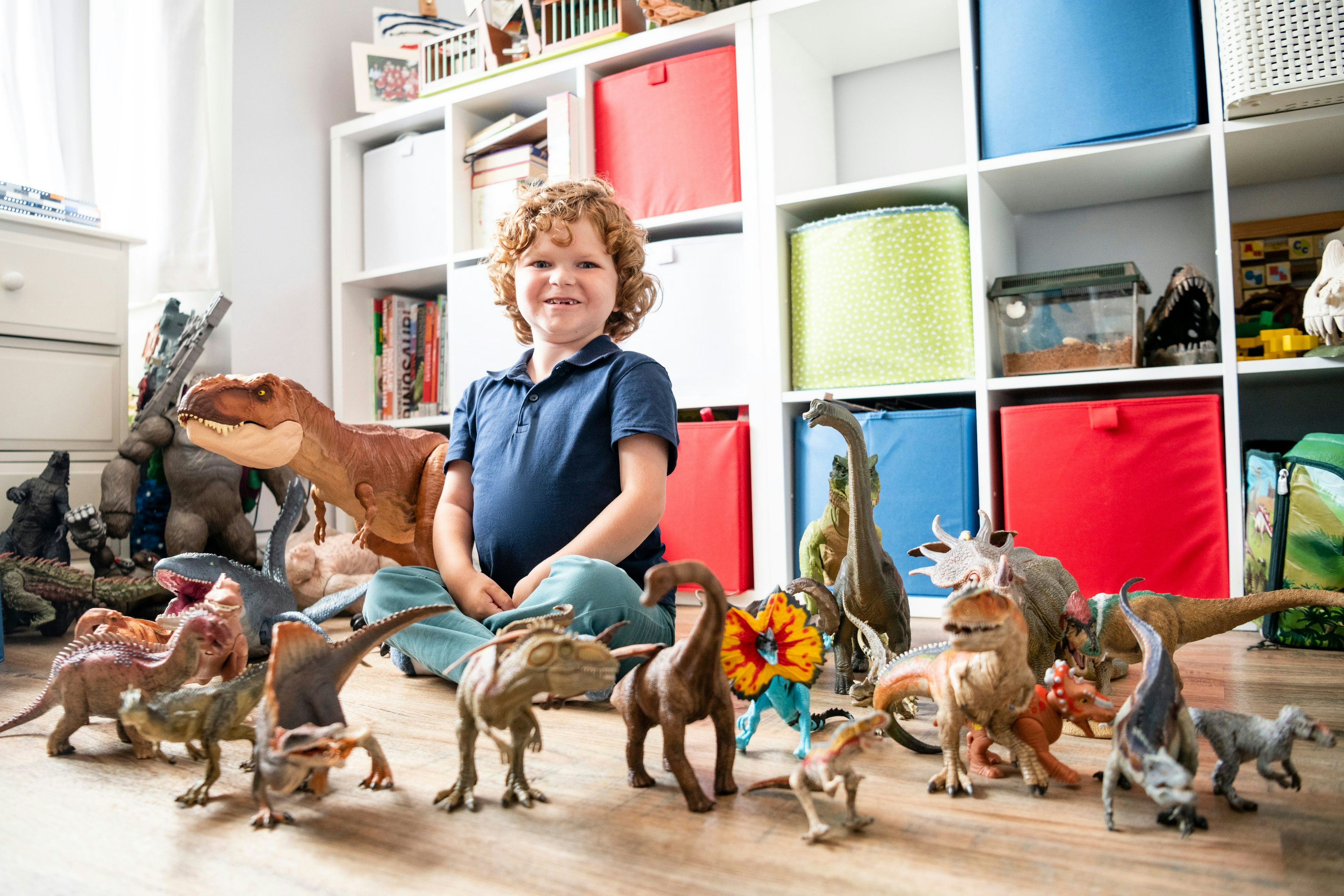 A little boy sits surrounded by toy dinosaurs.