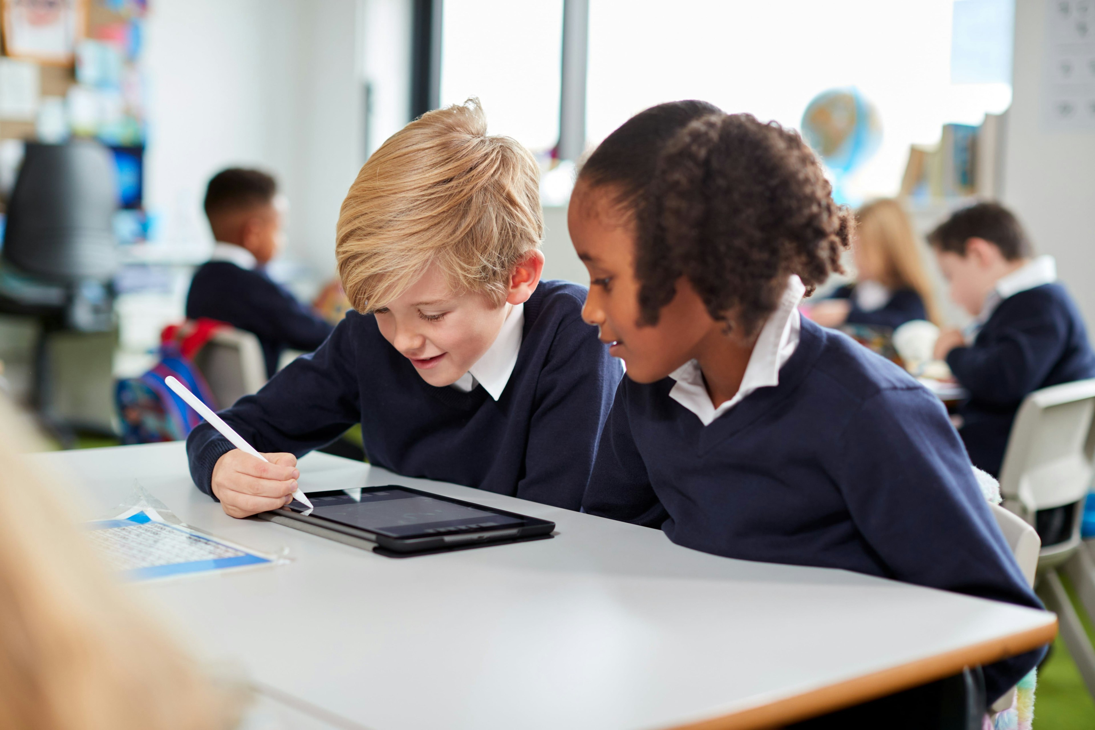 Two schoolchildren write on a tablet.