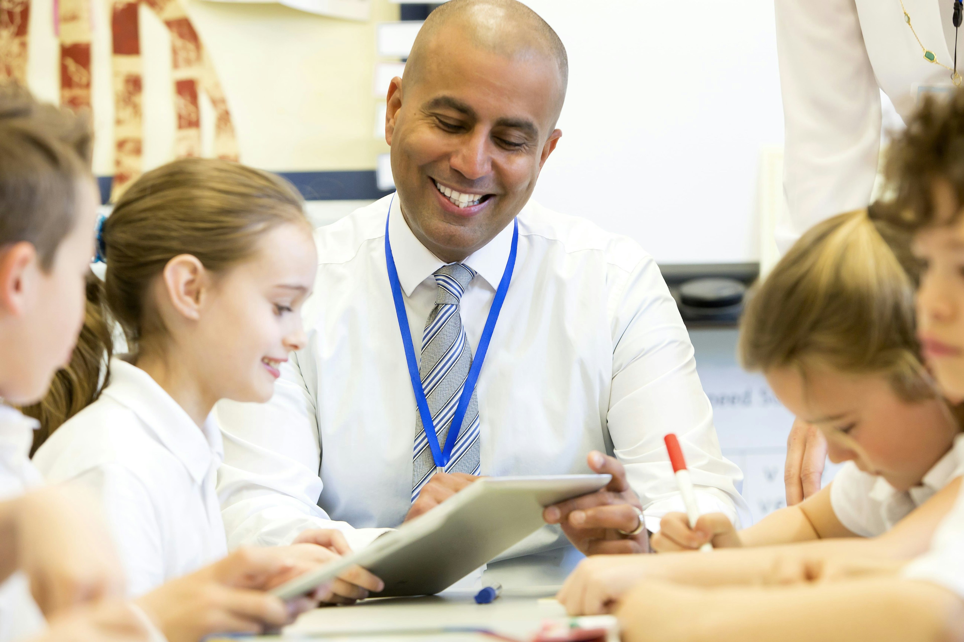 A smiling teachers shows pupils a tablet screen.